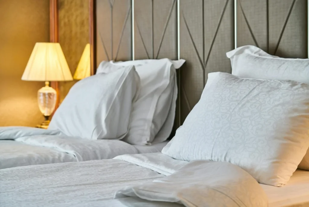 Close-up of a mattress with white bedding and pillows against an upholstered headboard