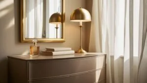 Bedroom corner with gold bedroom accessories like mirror, lamp, and soft dresser styling.