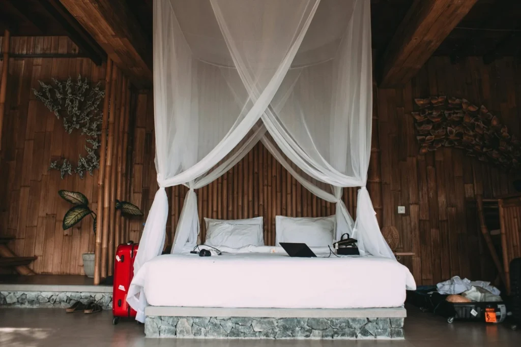 Four-poster bed draped in flowing white netting inside a rustic wooden bedroom