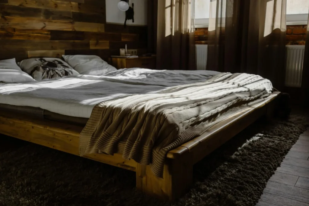 Low wooden double bed with rumpled blankets in a cozy wood-panelled bedroom