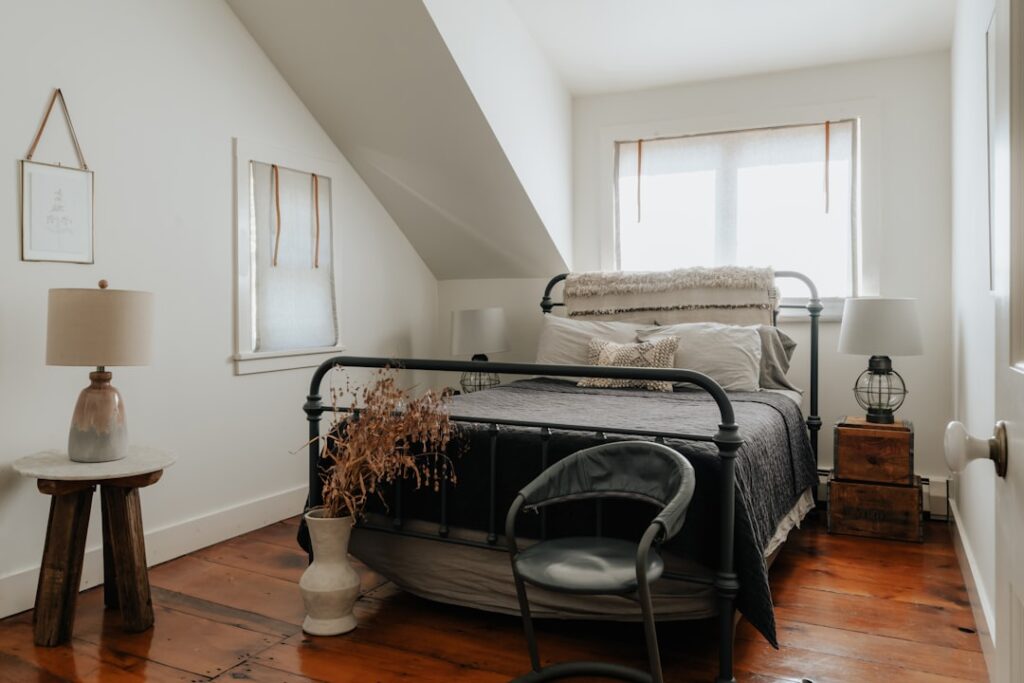 Black metal bed frame with slatted headboard in a bright attic bedroom with wood floors