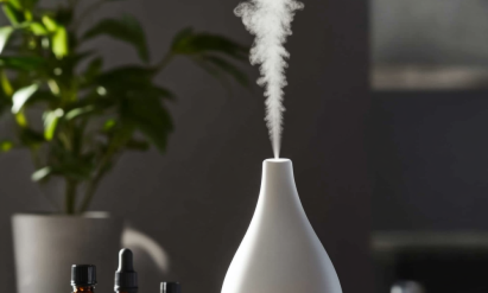 A diffuser in use, releasing a fine mist of essential oil, with bottles and greenery for ambiance